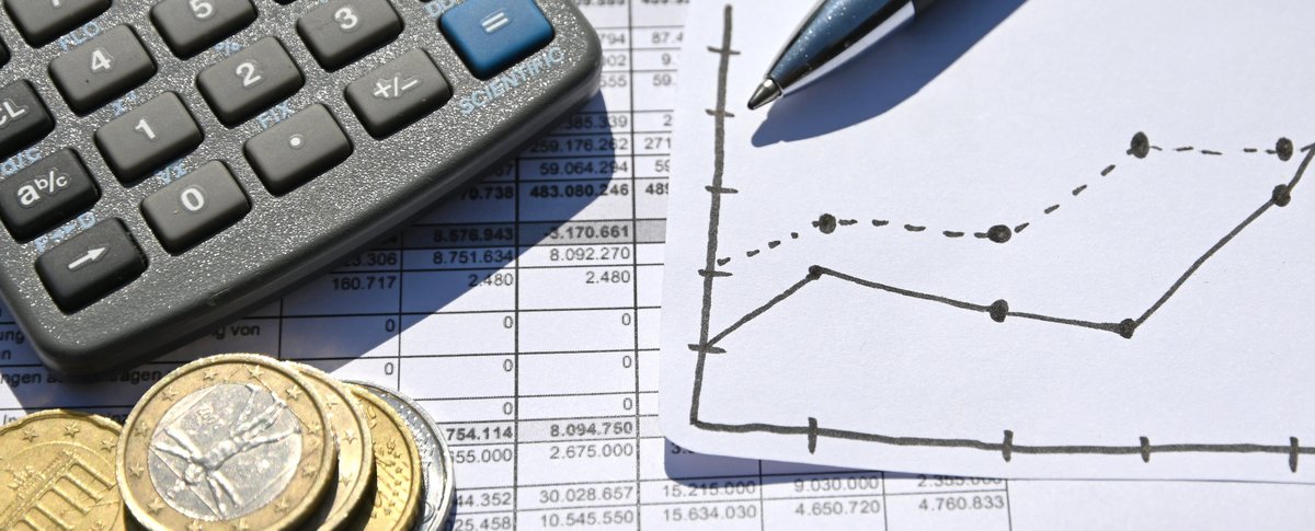 Auf einem Ausdruck einer Tabelle mit Zahlen liegen Münzen, ein Taschenrechner, ein Kugelschreiber und eine gezeichnete Grafik. Foto: Judith Wedderwille/ Kreis Soest