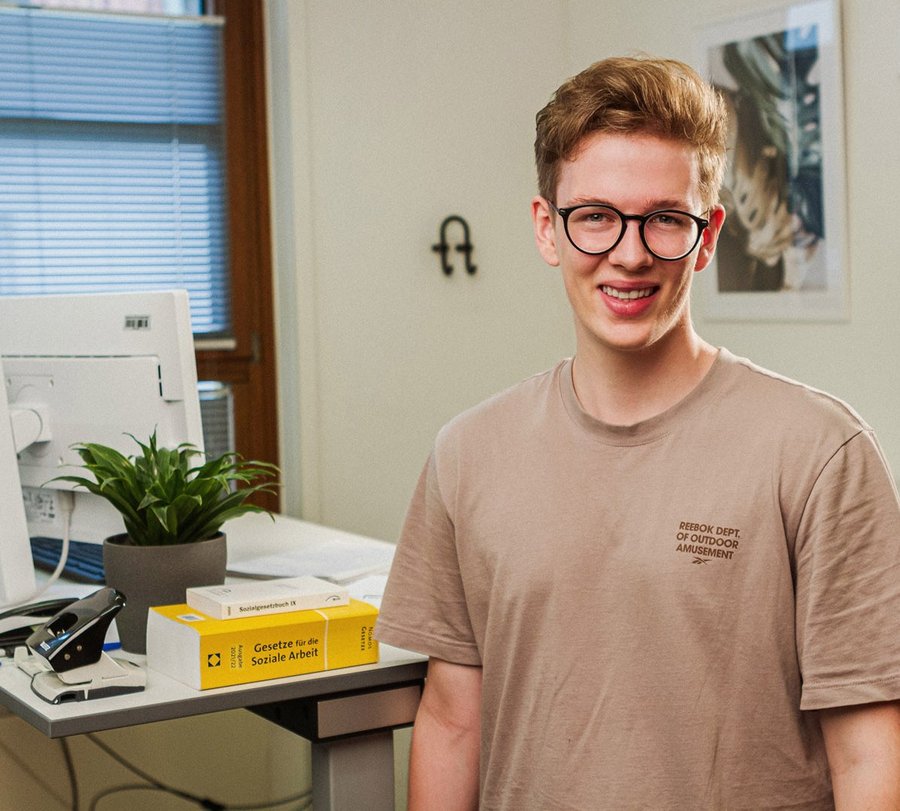 Ein junger Mann steht vor einem Schreibtisch mit Lektüre zu Sozialer Arbeit. Foto: Thomas Grimm