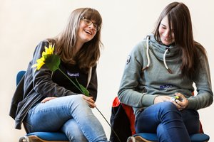 Zwei junge Frauen auf Stühlen mit einem Lächeln im Gesicht. Foto: © Irrsinnig Menschlich
