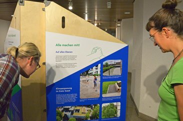 Bei Personen betrachten den Aufsteller zur Ausstellung „Aufgepasst. Angepasst!“. Foto: Kira Hönicke/ Kreis Soest