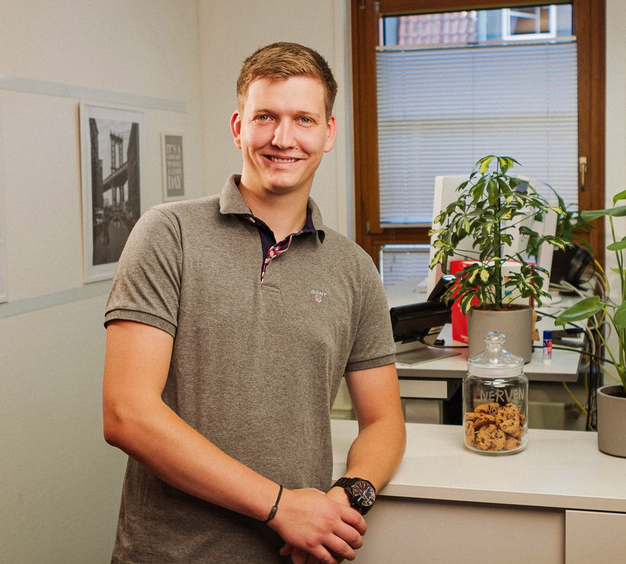 Verwaltungsfachangestellter. Foto: Thomas Grimm Ein Mann steht angelehnt vor einem Sideboard im Büro. Foto: Thomas Grimm