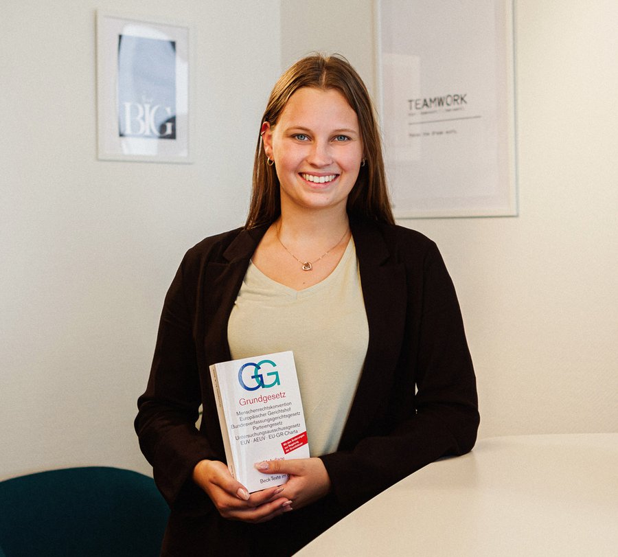 Bachelor of Laws - Kommunaler Verwaltungsdienst. Foto: Thomas Grimm Eine junge Frau steht mit einem Grundgesetz an einem modernen Besprechungstisch vor einem Whiteboard. Foto: Thomas Grimm