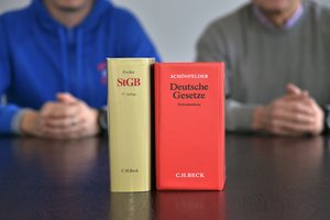 Zwei Gesetzesbücher auf einem Tisch, dahinter sitzen zwei Menschen. Foto: Thomas Weinstock/Kreis Soest