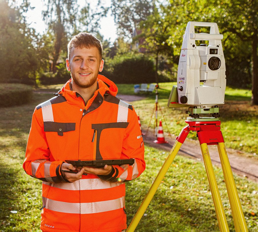 Vermessungstechniker. Foto: Thomas Grimm Ein junger Mann steht neben typischen Vermessungsgeräten draußen im Grünen und hält ein Tablet.Foto: Thomas Grimm