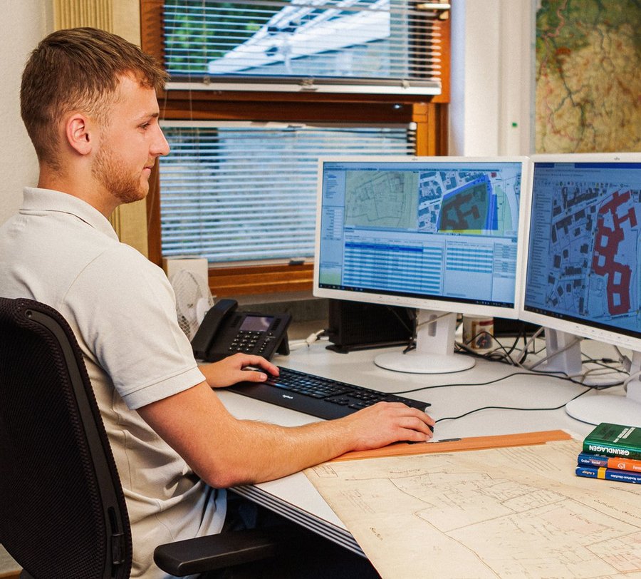 Ein junger Mann schaut auf seinen Bildschirm. Neben ihm liegt eine Vermessungskarte. Foto: Thomas Grimm