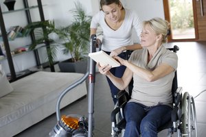 Junge Frau hilft Frau im Rollstuhl bei Hausarbeit. Foto: © goodluz - Fotolia.com