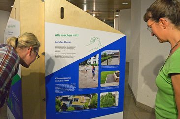 Bei Personen betrachten den Aufsteller zur Ausstellung „Aufgepasst. Angepasst!“. Foto: Kira Hönicke/ Kreis Soest