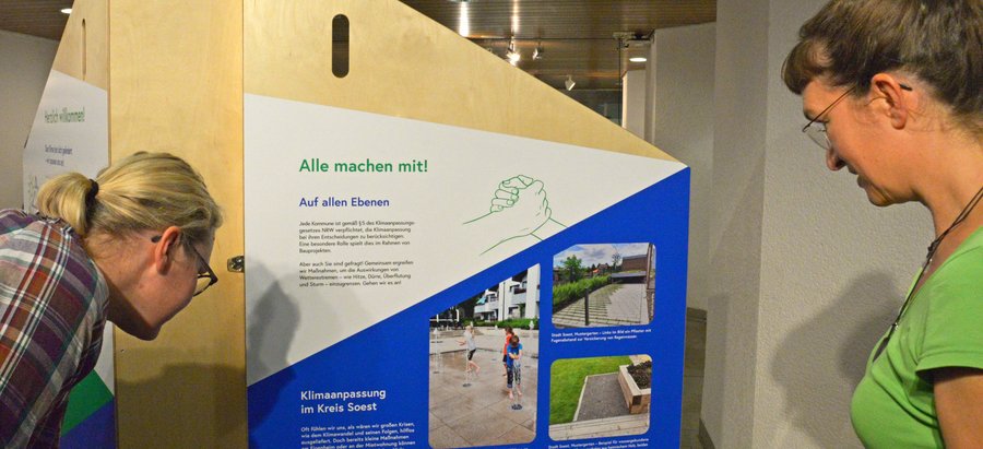 Bei Personen betrachten den Aufsteller zur Ausstellung „Aufgepasst. Angepasst!“. Foto: Kira Hönicke/ Kreis Soest