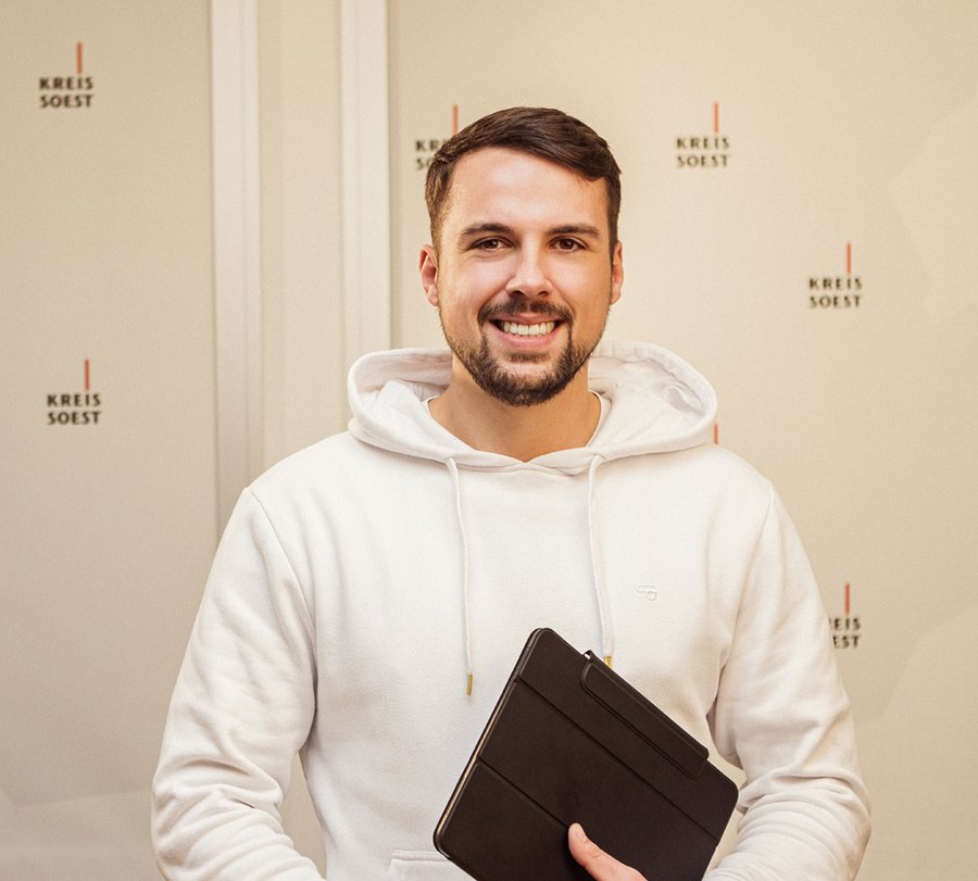 Volontär für die Presse- und Öffentlichkeitsarbeit. Foto: Thomas Grimm Ein Mann steht vor einer Wand, auf der im Hintergrund viele "Kreis Soest"-Logos zu sehen sind. Foto: Thomas Grimm