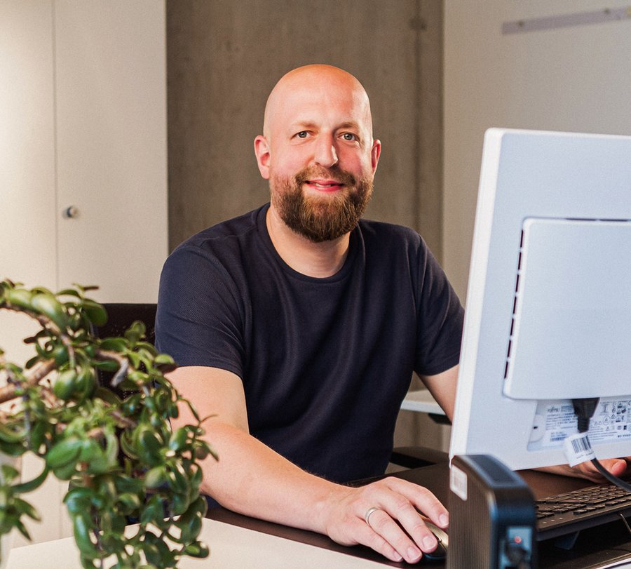 Verwaltungswirt. Foto: Thomas Grimm Ein Mann sitzt vor einem PC und lächelt in die Kamera. Foto: Thomas Grimm