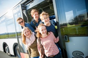 Fünf Kinder und Jugendliche stehen in der Tür eines Busses und schauen nach vorn. Foto: RLG