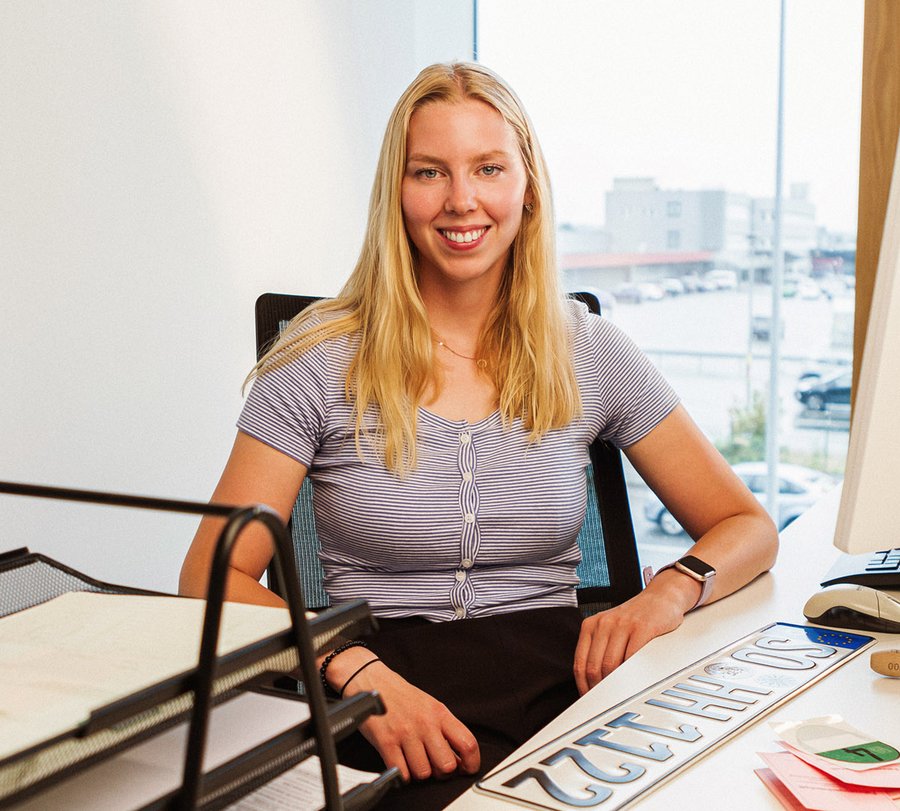 Kaufleute für Büromanagement. Foto: Thomas Grimm Eine junge Frau sitzt vor einem KFZ-Kennzeichen am Platz und lächelt in die Kamera. Foto: Thomas Grimm
