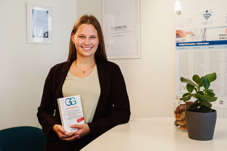 Bachelor of Laws - Kommunaler Verwaltungsdienst. Foto: Thomas Grimm Eine junge Frau steht mit einem Grundgesetz an einem modernen Besprechungstisch vor einem Whiteboard. Foto: Thomas Grimm