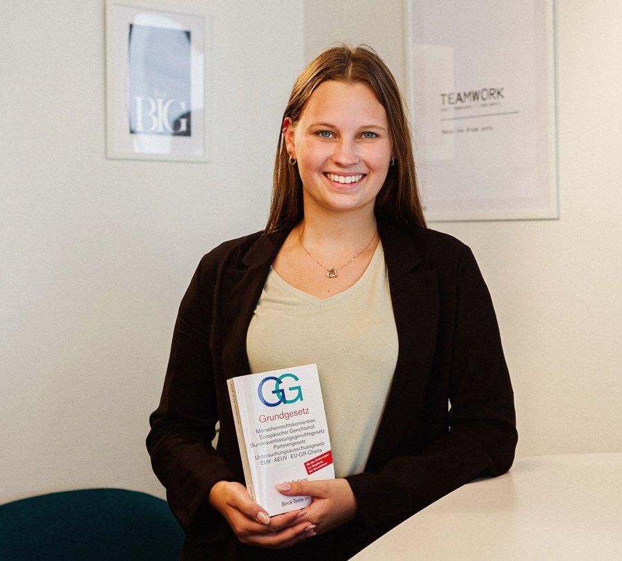 Eine junge Frau steht mit einem Grundgesetz an einem modernen Besprechungstisch vor einem Whiteboard. Foto: Thomas Grimm