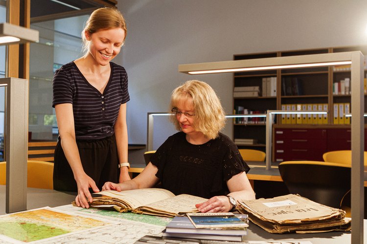 Eine Frau berät eine andere Frau zu alten Unterlagen des Kreisarchivs, die vor ihr ausgebreitet sind. Foto: Thomas Grimm