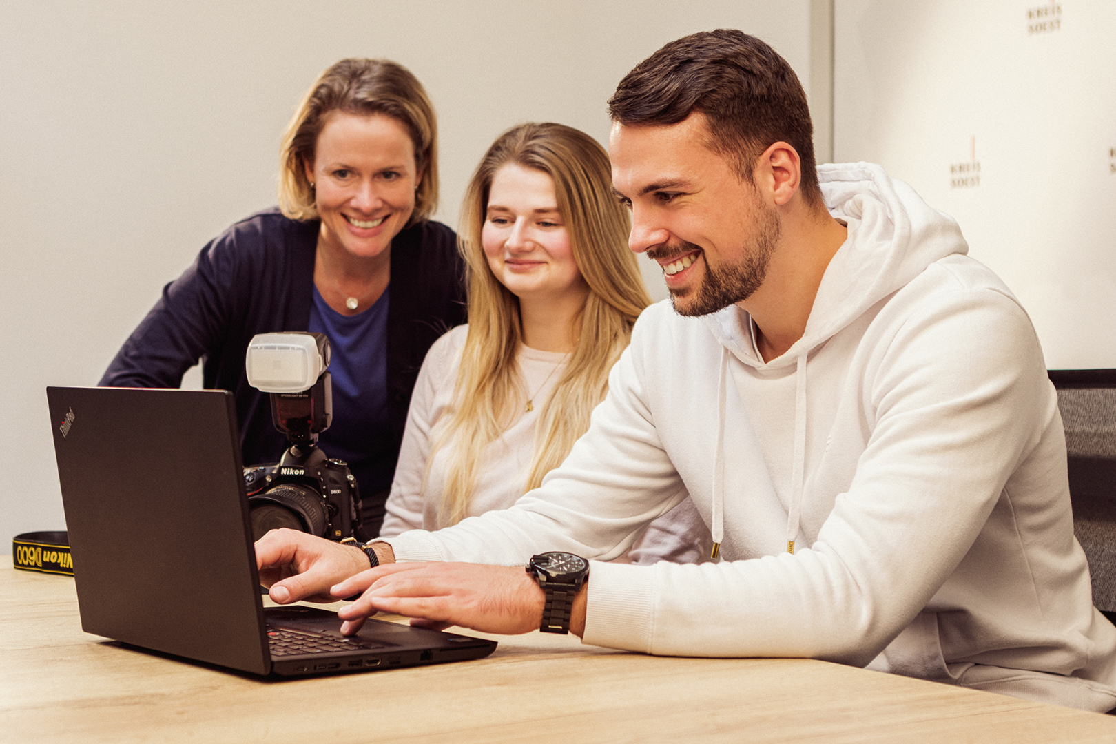 Eine Person schaut lächelnd auf einen Laptop. Zwei weitere Personen schauen ebenfalls auf den Laptop. Foto: Thomas Grimm